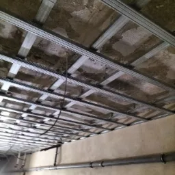 Metalowa konstrukcja sufitu podwieszanego w trakcie montażu w Jemielnie, widoczne rury instalacyjne przy ścianie.