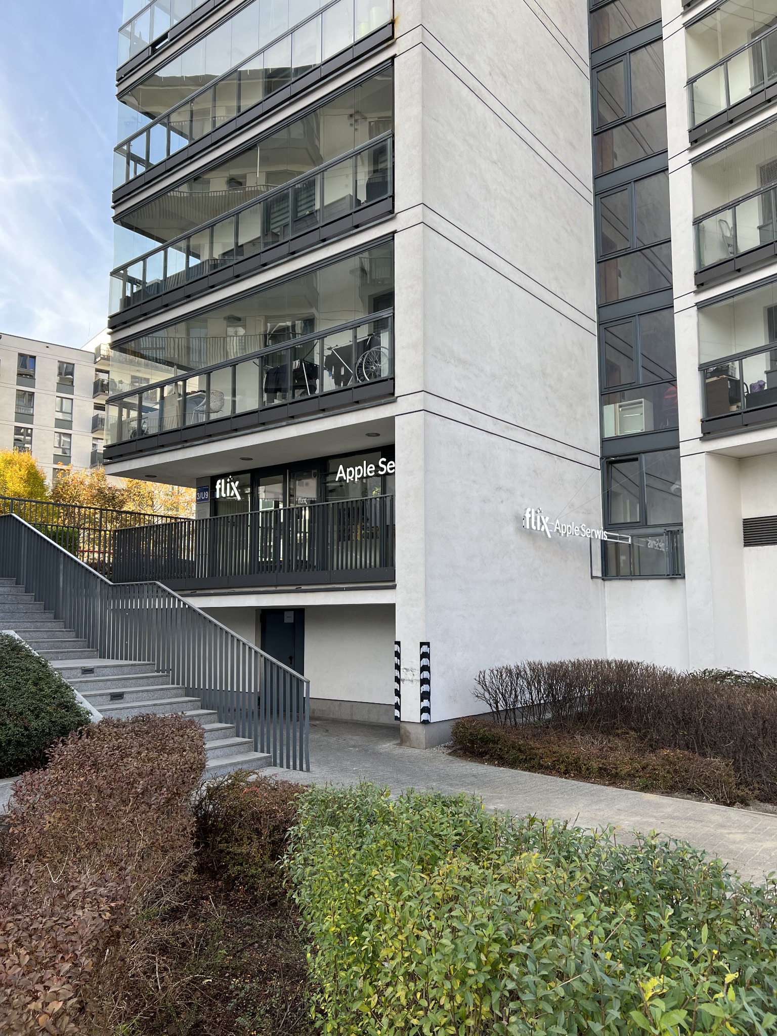 Budynek usługowy z napisem 'flix Apple Serwis' oraz schodami wejściowymi, widok z zewnątrz.