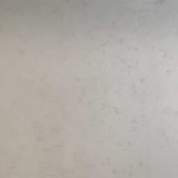 Mariusz Łady - Ściana pokryta szarą, dekoracyjną fakturą imitującą beton, z widocznym wiadrem farby Jeger Beton i zabezpieczoną folią podłogą.