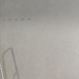 Mariusz Łady - Ściana pokryta szarą, dekoracyjną masą betonową, widoczne puszki farby Jeger Beton, zabezpieczona folią podłoga i drabina oparta o ścianę.