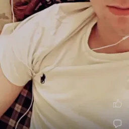 Młody mężczyzna w okularach i białej koszulce z logo, słuchający muzyki na słuchawkach, widok z góry.