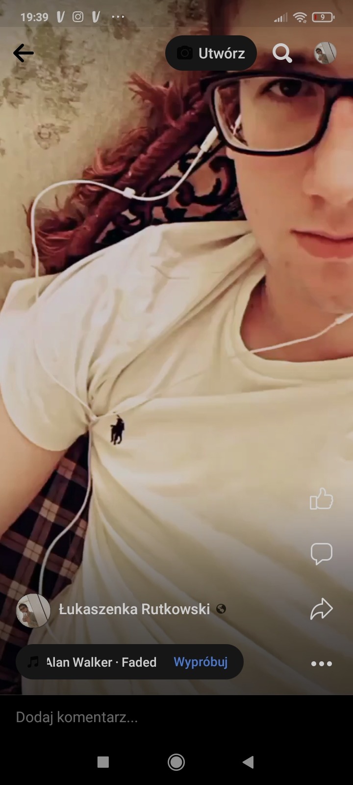 Młody mężczyzna w okularach i białej koszulce z logo, słuchający muzyki na słuchawkach, widok z góry.