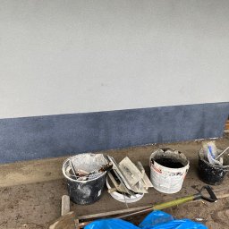 Usługi Budowlane Artur Ochodek - Dwuwarstwowa elewacja budynku z widocznymi narzędziami i wiadrami z zaprawą gotowymi do dalszych prac wykończeniowych.