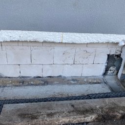 Usługi Budowlane Artur Ochodek - Fragment ściany zewnętrznej budynku z widocznym ociepleniem styropianem, bloczkami betonowymi i fragmentem elewacji w trakcie prac wykończeniowych.