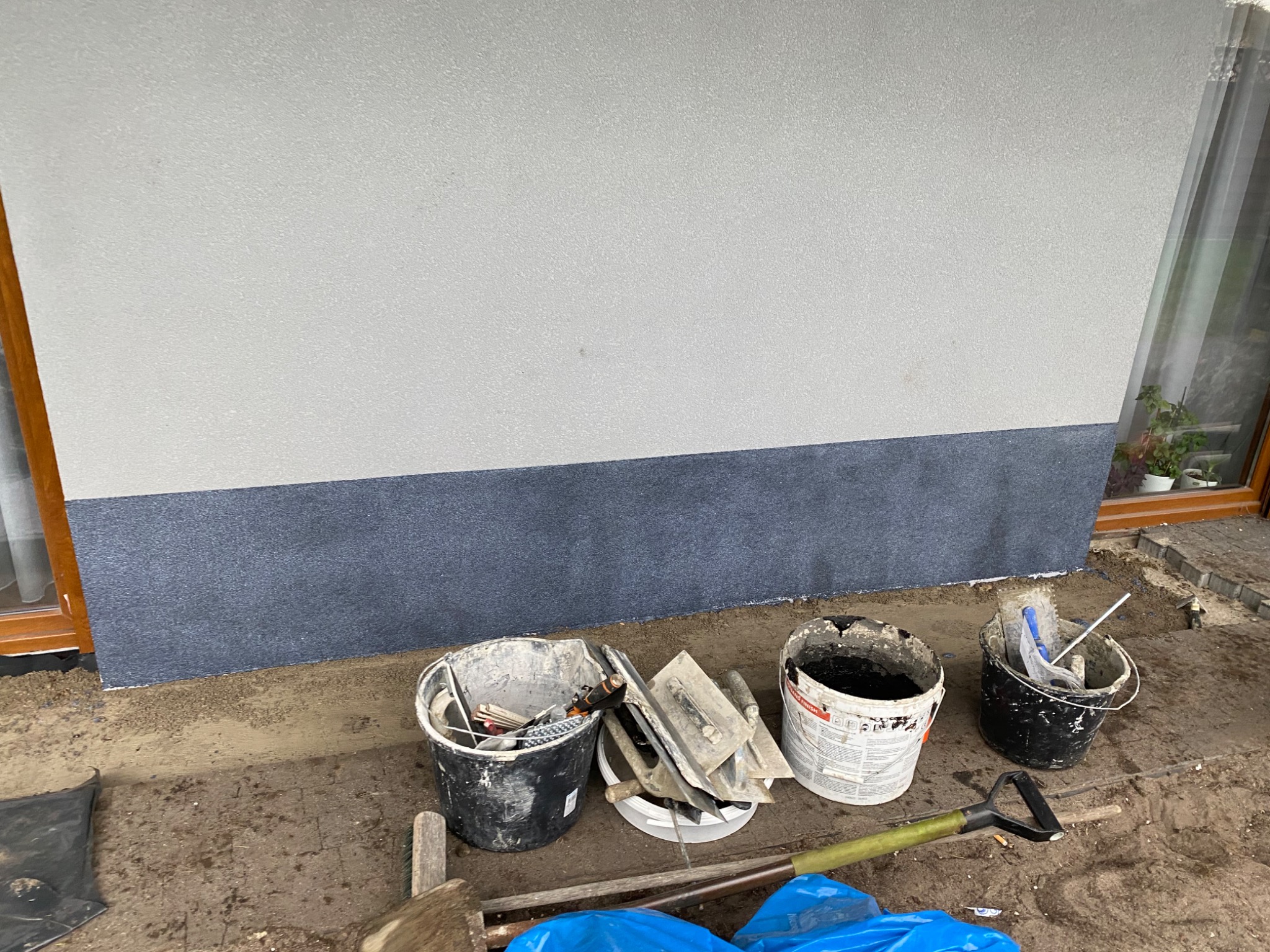 Dwuwarstwowa elewacja budynku z widocznymi narzędziami i wiadrami z zaprawą gotowymi do dalszych prac wykończeniowych.