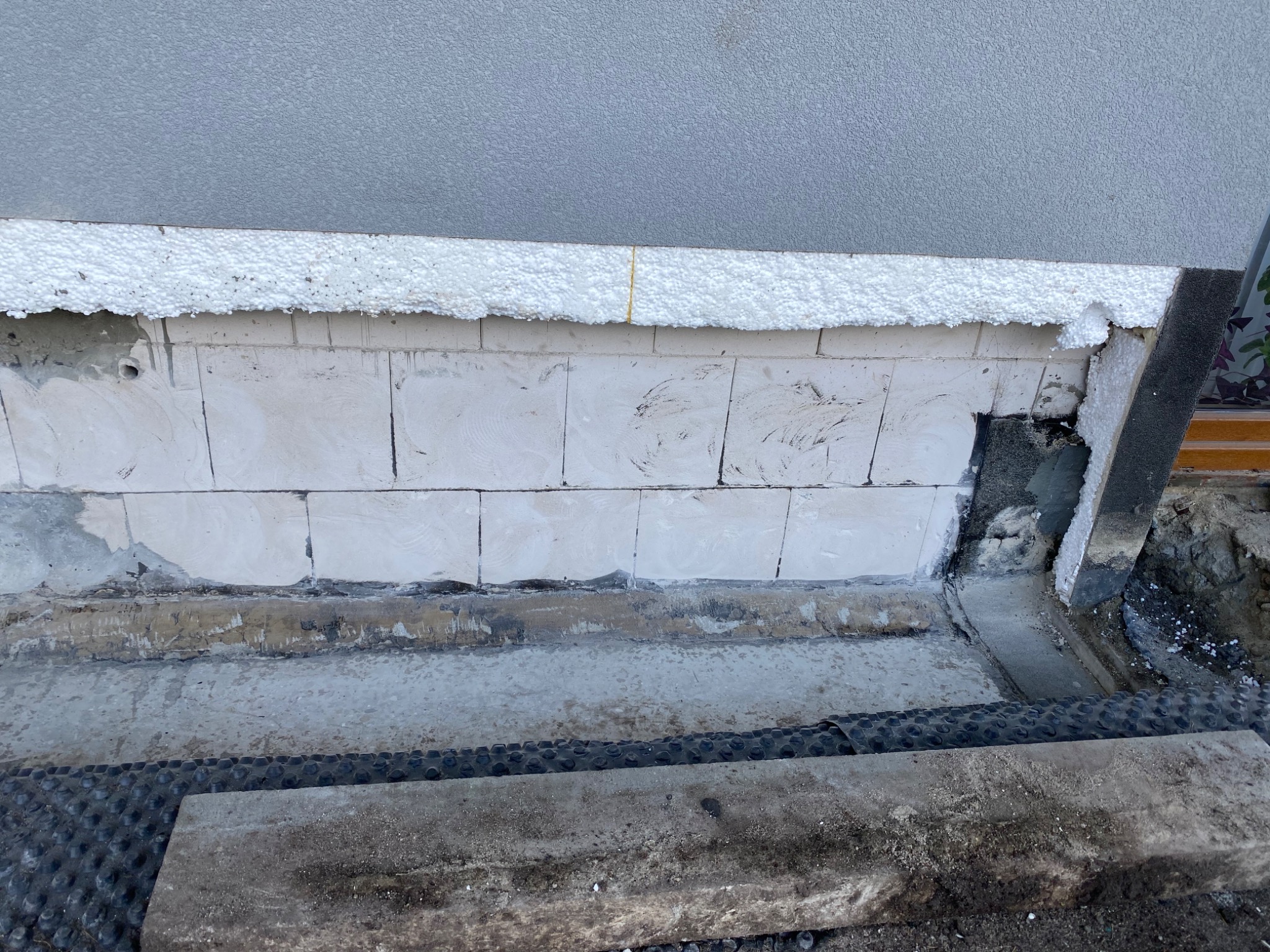 Fragment ściany zewnętrznej budynku z widocznym ociepleniem styropianem, bloczkami betonowymi i fragmentem elewacji w trakcie prac wykończeniowych.