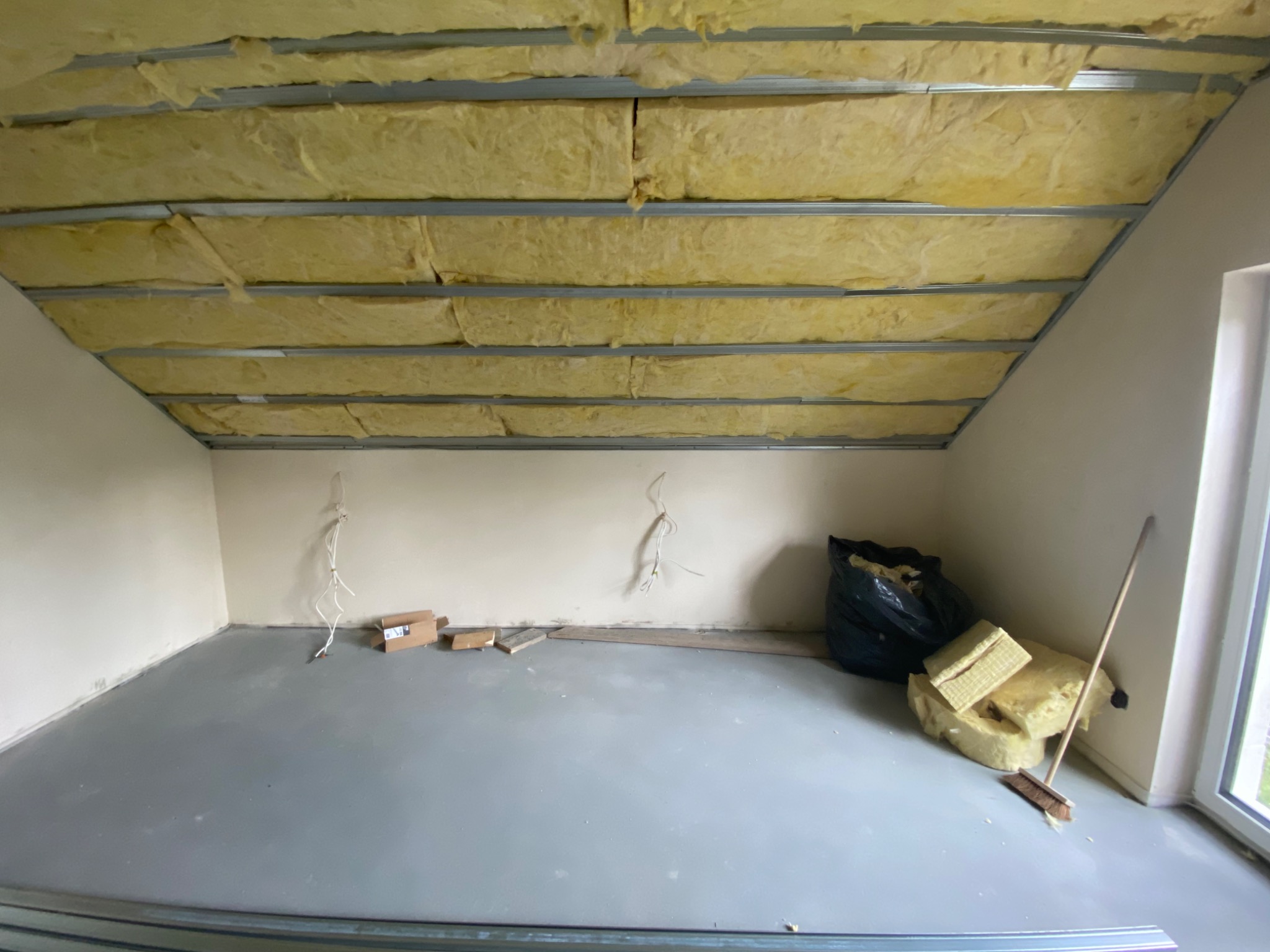 Poddasze w trakcie ocieplania wełną mineralną w Krakowie, widoczne metalowe profile pod konstrukcję sufitu, resztki materiału i śmieci na podłodze.