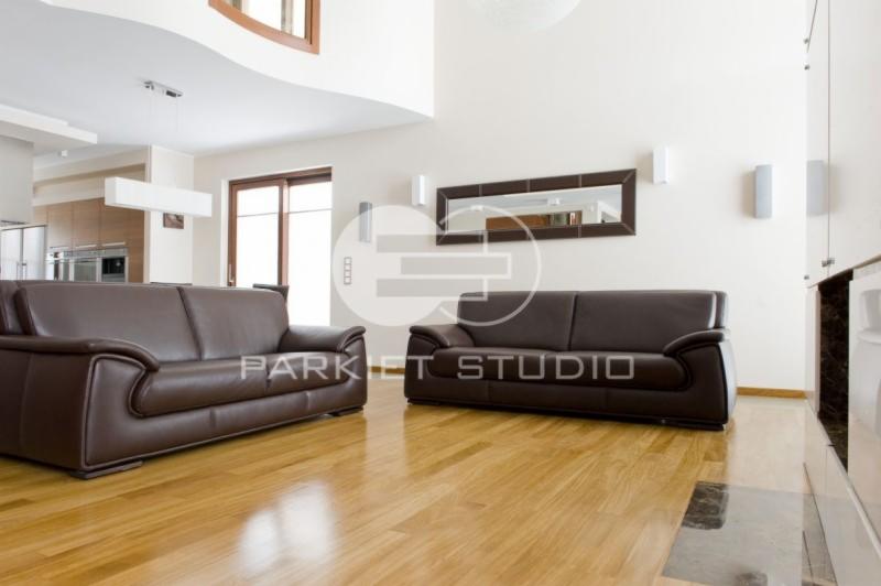 Salon z jasną, lakierowaną podłogą z drewna egzotycznego Iroko, dwoma brązowymi skórzanymi sofami i nowoczesnym oświetleniem.