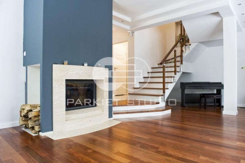 Salon z parkietem Merbau, kominkiem obłożonym trawertynem i schodami z drewnianymi stopniami oraz fortepianem w tle.