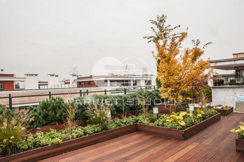 Cumaru deski tarasowe na dachu budynku z zielenią w donicach, widok na miasto w tle.