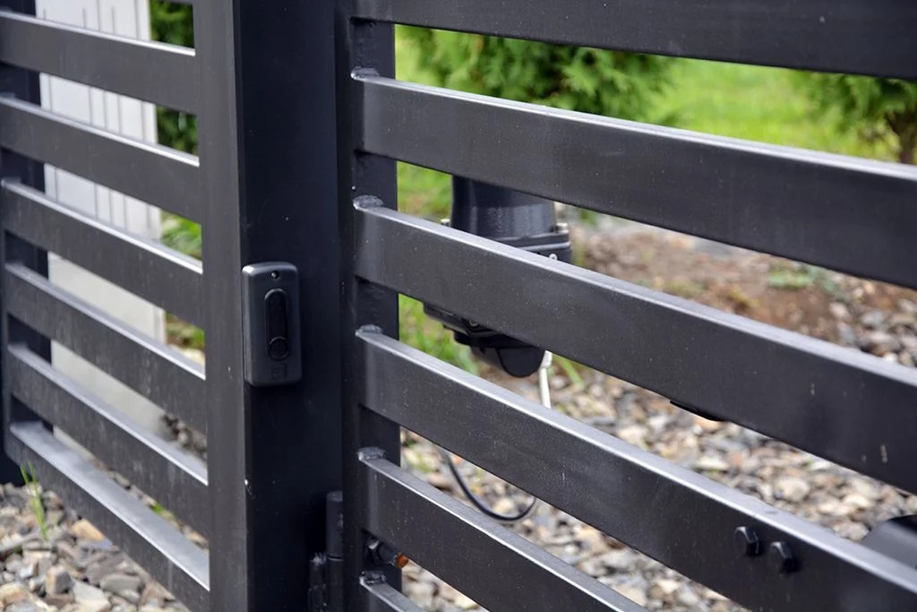 Nowoczesna, czarna brama wjazdowa z automatyką i czytnikiem zbliżeniowym, widok z bliska na mechanizm i elementy sterujące.