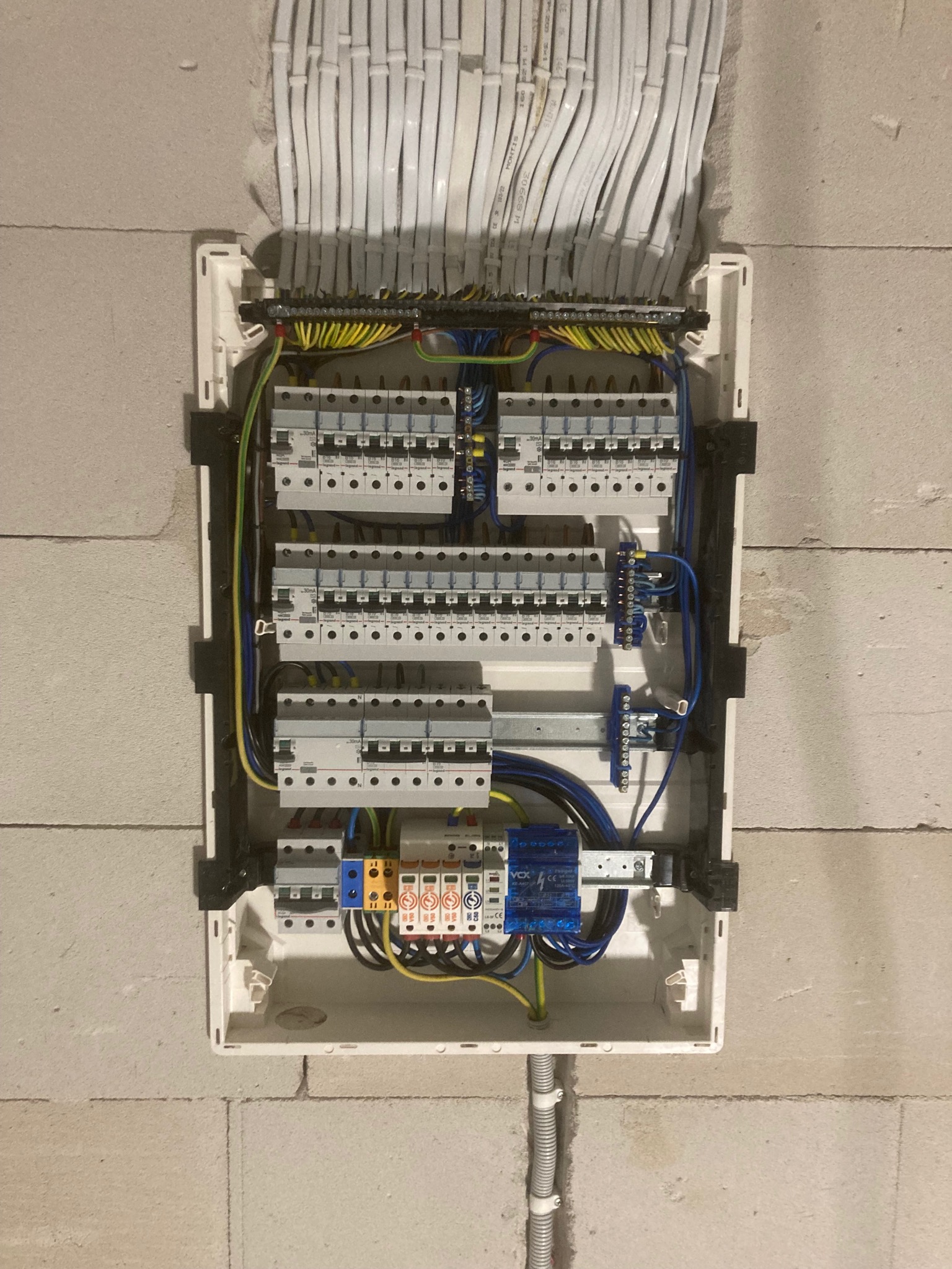 Rozdzielnica elektryczna w trakcie montażu w surowej ścianie z betonu komórkowego, widoczne liczne przewody, bezpieczniki i elementy instalacji elektrycznej.