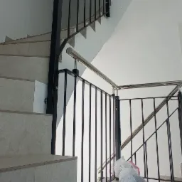 Wewnętrzna klatka schodowa z czarną metalową balustradą i stalową poręczą, widoczne worki z odpadami po montażu.