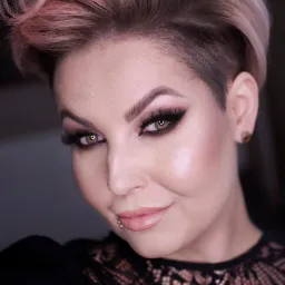 Portret kobiety z profesjonalnym makijażem smokey eye, podkreślonymi brwiami, błyszczącymi ustami i asymetryczną fryzurą w odcieniach blondu i różu, noszącej czarną koronkową bluzkę i kolczyk...