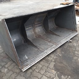 Zakład Tokarsko Ślusarski Igański Mirosław - Surowy, spawany metalowy kosz ładowarki na zewnątrz, widoczne spawy i konstrukcja wzmacniająca, na tle kostka brukowa i zabudowania.