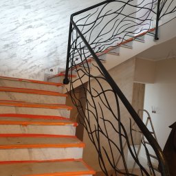 Zakład Tokarsko Ślusarski Igański Mirosław - Marmurowe schody z czarną, dekoracyjną balustradą o motywie gałęzi, zabezpieczone folią ochronną podczas remontu.