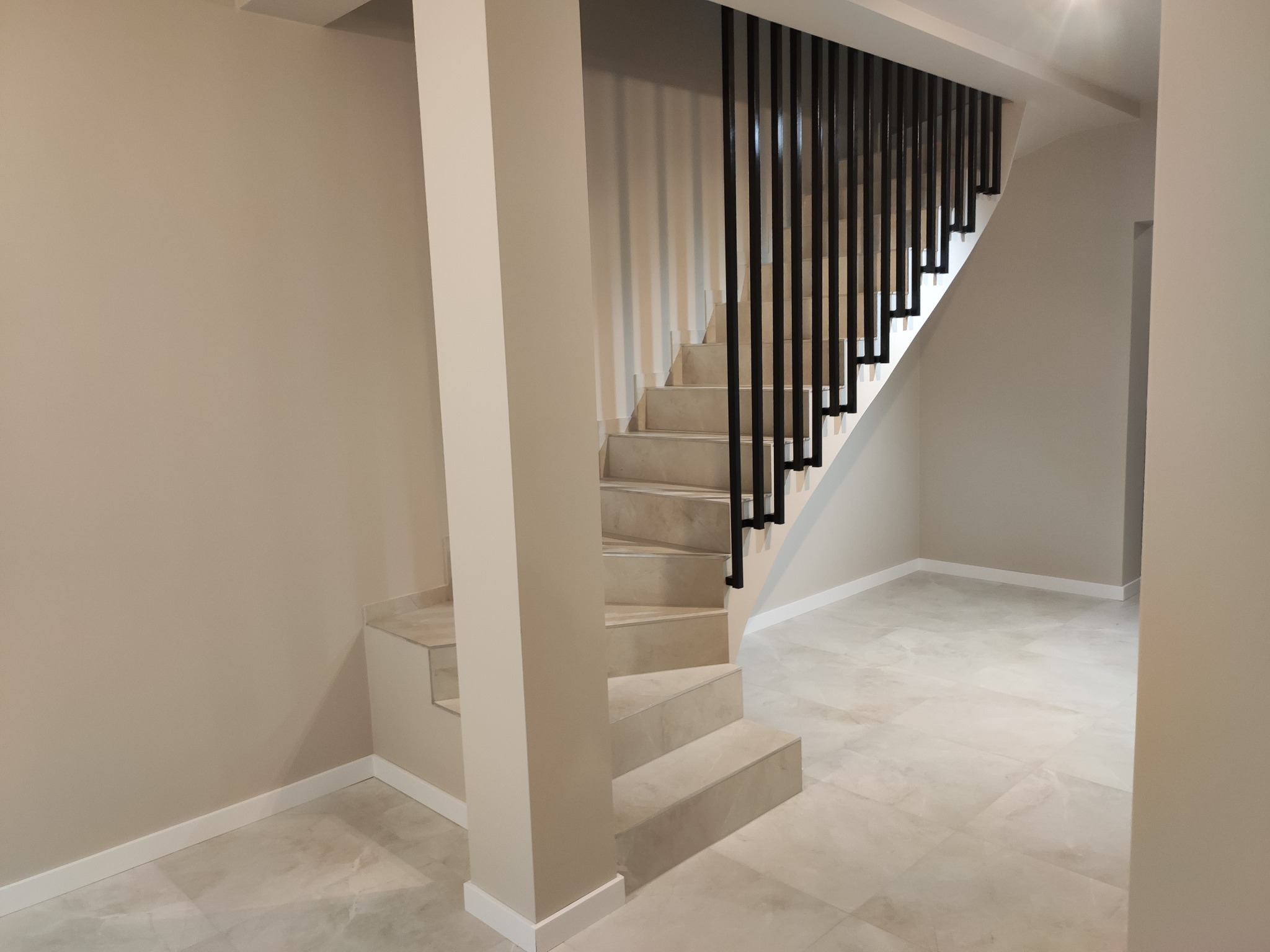 Jasne, wykafelkowane schody z czarną, minimalistyczną balustradą w nowoczesnym wnętrzu, widok z dołu.