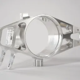 Precyzyjnie obrobiony, surowy, aluminiowy odlew z licznymi otworami i mocowaniami, sfotografowany na jasnym tle.