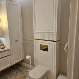 StarBud - Elegancka łazienka w odcieniach bieli i złota: zabudowana toaleta z szafką, marmurowe płytki podłogowe, detale dekoracyjne. Nowoczesny design z luksusowymi akcentami.