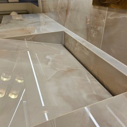 StarBud - Beżowa, marmurkowa umywalka w łazience, z widocznymi refleksami światła. Umywalka zintegrowana z blatem, wykonana z płytek. Minimalistyczny design, eleganckie wykończenie.