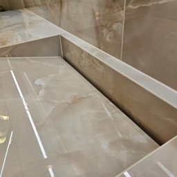 StarBud - Beżowe, polerowane płytki imitujące marmur, ułożone w geometryczny wzór na ścianie i blacie. Widoczne fugi i odbicie światła, podkreślające gładką powierzchnię.