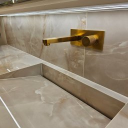 StarBud - Beżowa umywalka z marmurowym wzorem i złotą armaturą ścienną. Minimalistyczny design, oświetlenie LED podkreśla elegancję wykończenia.