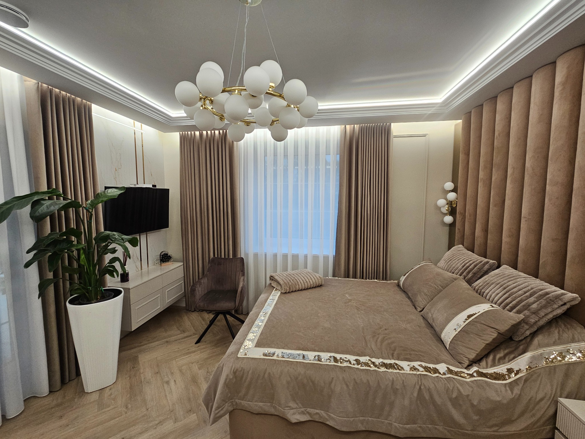 Elegancka sypialnia w beżach: tapicerowane panele ścienne, designerska lampa, drewniana podłoga i dekoracyjne zasłony. Nowoczesne wykończenie wnętrza.