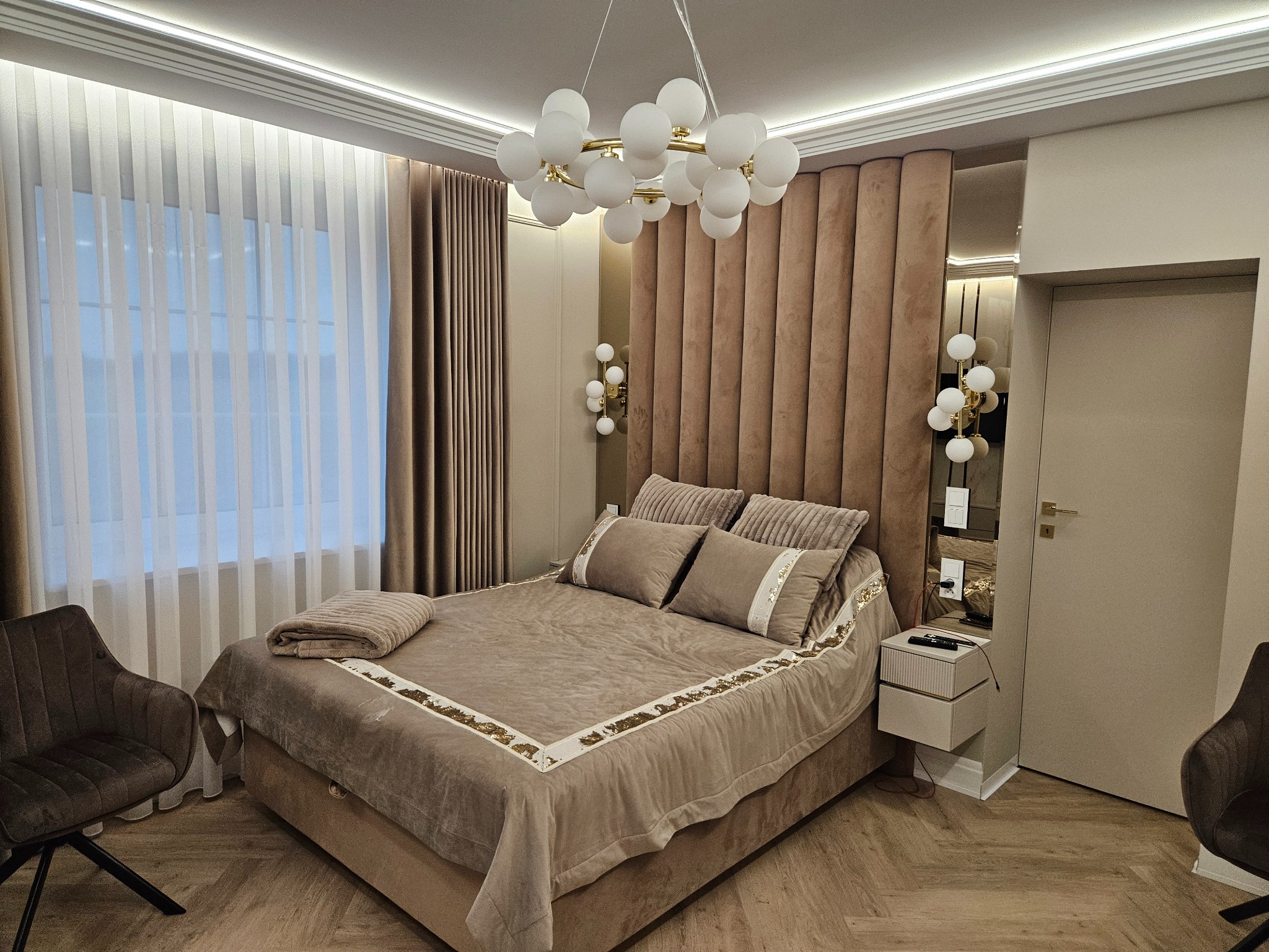 Elegancka sypialnia w beżach: tapicerowane wezgłowie, designerska lampa, parkiet w jodełkę. Nowoczesne wykończenie wnętrza z dbałością o detale i komfort.