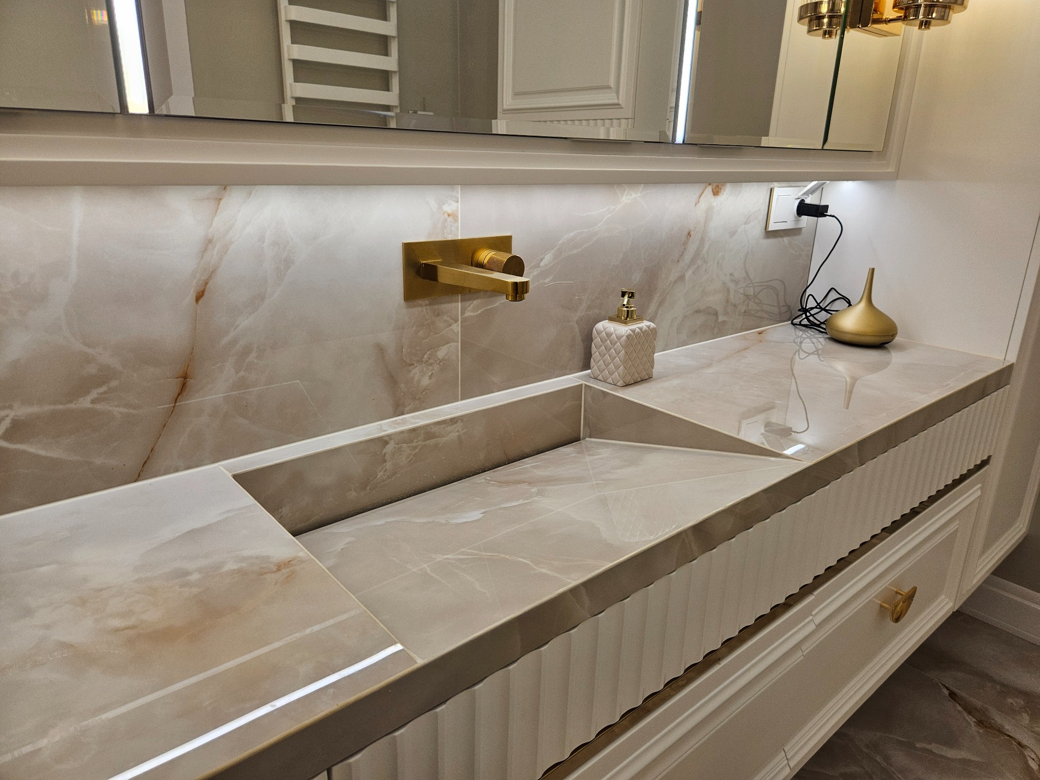 Elegancka łazienka: beżowa marmurowa umywalka z wbudowanym blatem, złota bateria i dekoracje. Nowoczesny design z subtelnym oświetleniem.