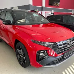 Czerwony Hyundai Tucson N Line z czarnym dachem i felgami, prezentowany w salonie samochodowym, z widocznym logo i charakterystycznym grillem.