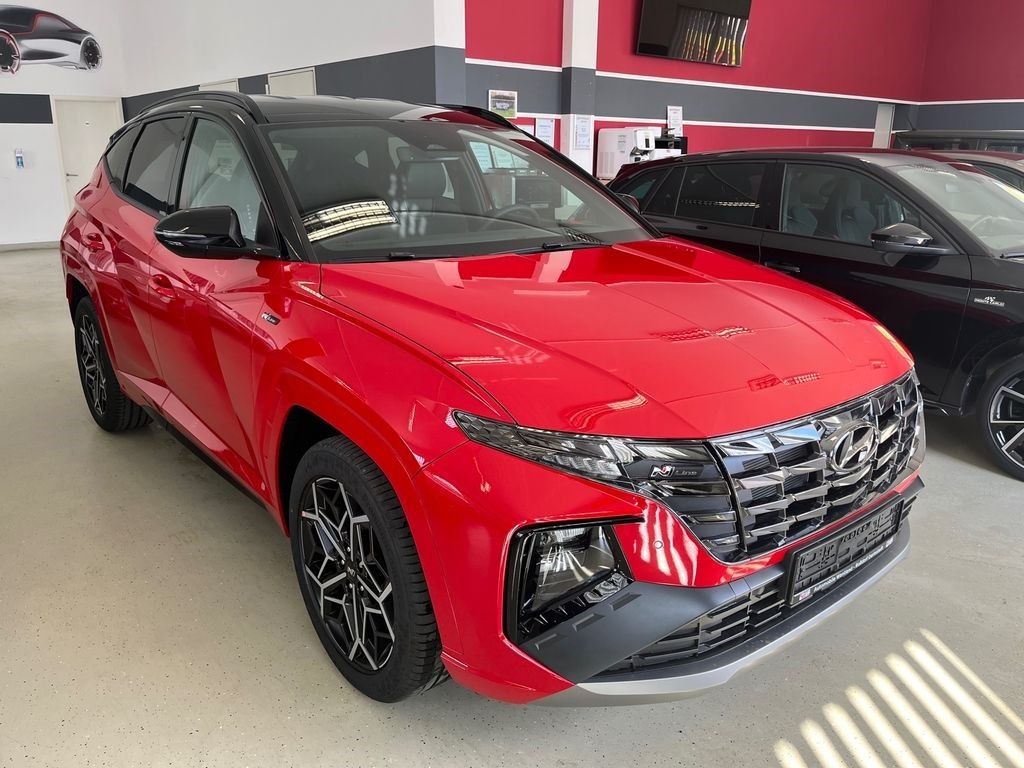 Czerwony Hyundai Tucson N Line z czarnym dachem i felgami, prezentowany w salonie samochodowym, z widocznym logo i charakterystycznym grillem.