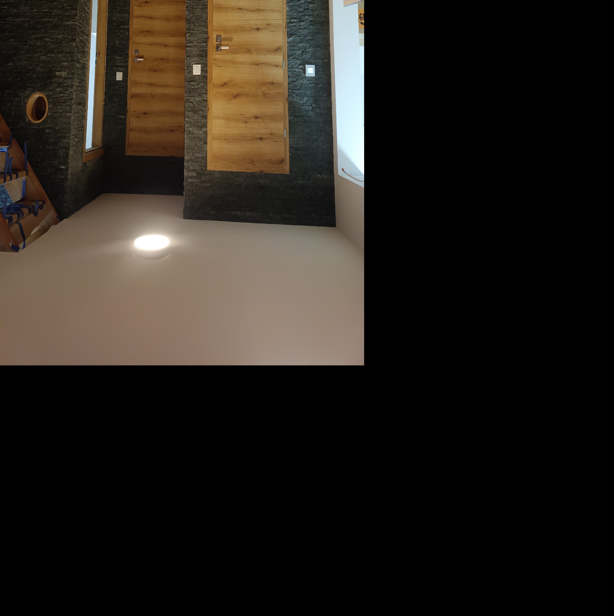 Dwa drewniane drzwi wewnętrzne z ościeżnicami wkomponowane w ścianę z czarnego kamienia łupkowego, oświetlone punktowym światłem sufitowym.