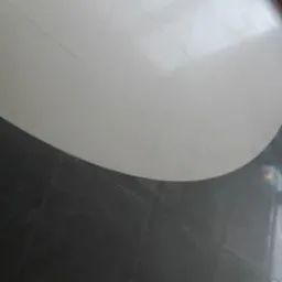 Biało-szara, błyszcząca podłoga z płytek ułożonych w łuk, widok z góry. Fragment okna w prawym górnym rogu. Minimalistyczny design podłogi w nowoczesnym wnętrzu.