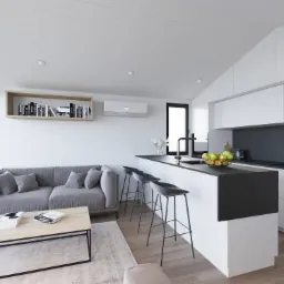 Wnętrze domu mobilnego: Szara sofa z poduszkami, drewniany stolik kawowy z książkami, wysokie stołki barowe przy białej wyspie kuchennej z czarnym blatem, owoce w misce, białe szafki kuchenne.