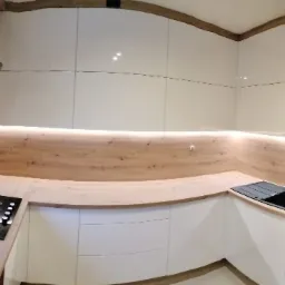 Nowoczesna kuchnia z białymi, błyszczącymi szafkami, drewnianym blatem podświetlonym listwą LED i czarną płytą grzewczą.