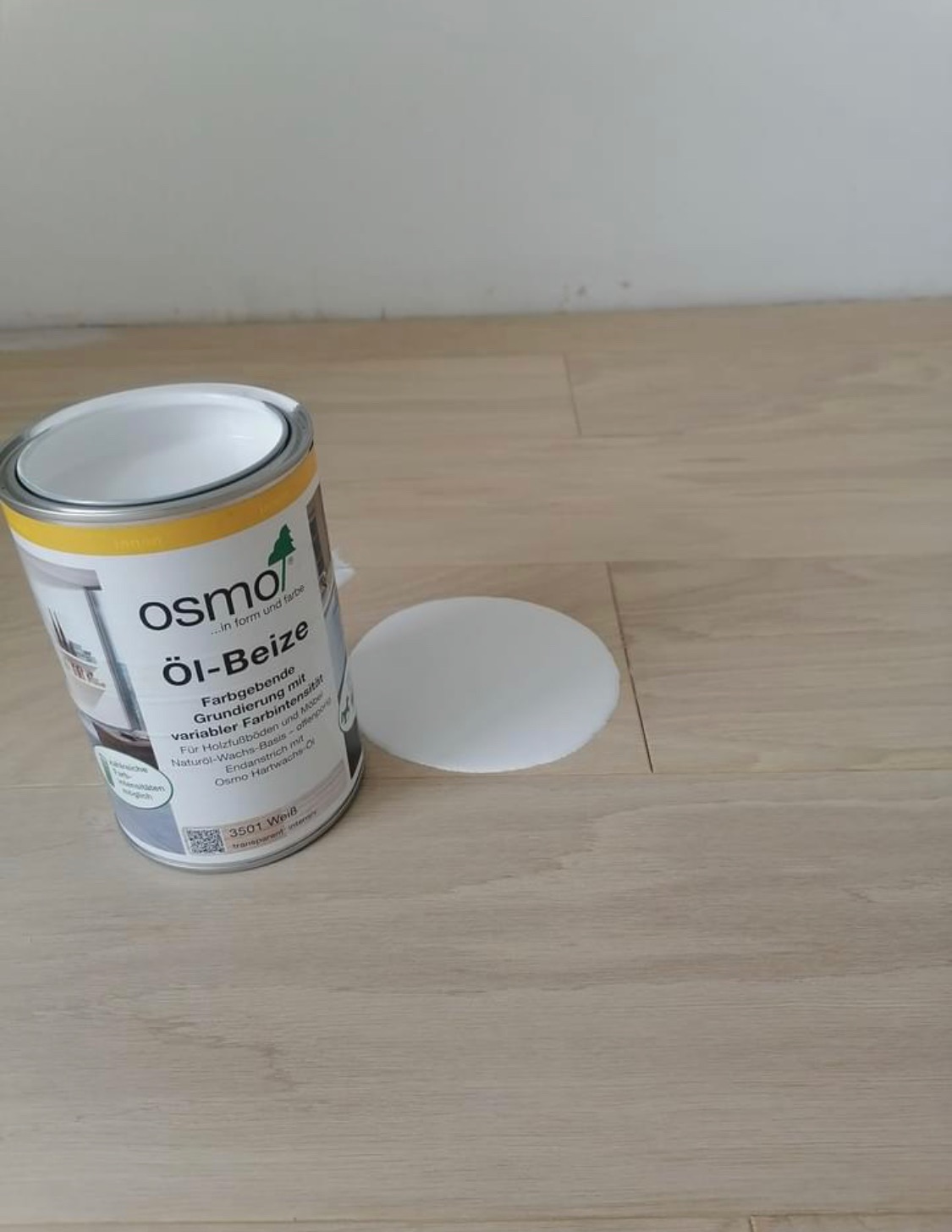 Puszka z bejcą olejną Osmo i biały aplikator na jasnej, drewnianej podłodze.