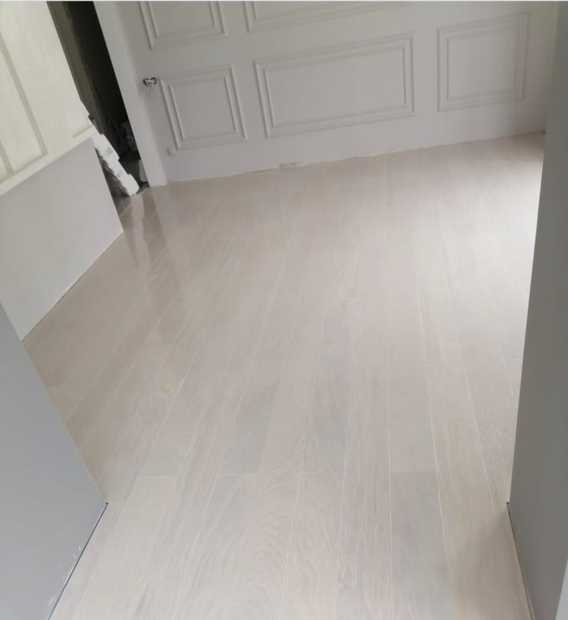 Jasna, lakierowana podłoga z drewnianych desek ułożona w nowym mieszkaniu, widoczne dekoracyjne listwy ścienne.