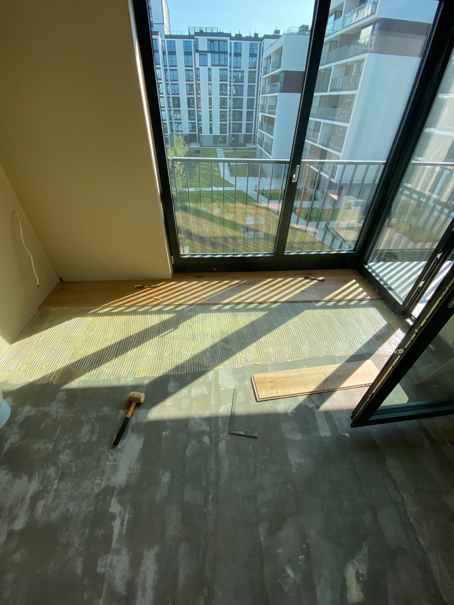 Układanie parkietu w nowym mieszkaniu z widokiem na osiedle; widoczny klej, parkiet, młotek i przymiar