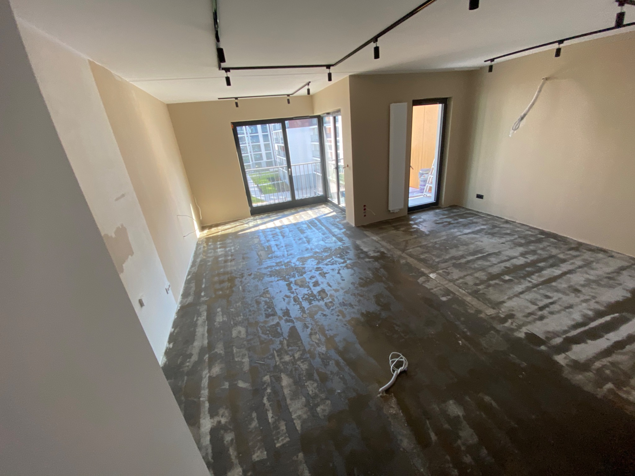 Wnętrze mieszkania w trakcie remontu, widoczna przygotowana powierzchnia podłoża, prawdopodobnie po usunięciu starej warstwy, z widocznymi śladami kleju lub szpachli, ściany częściowo pomalowane,...