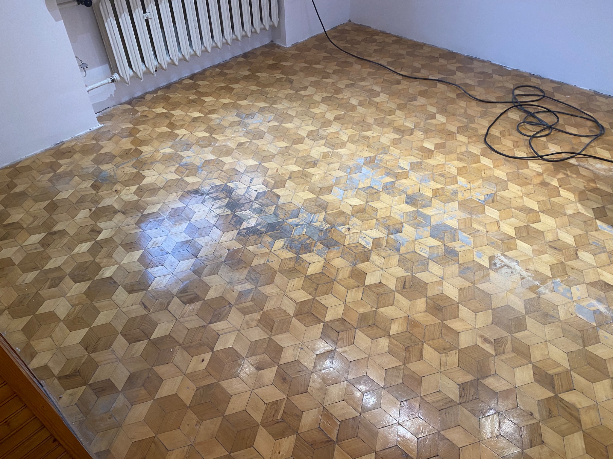 Parkiet w jodełkę 3D przed cyklinowaniem w Raszynie, widoczne ślady zużycia i kabel urządzenia do renowacji.