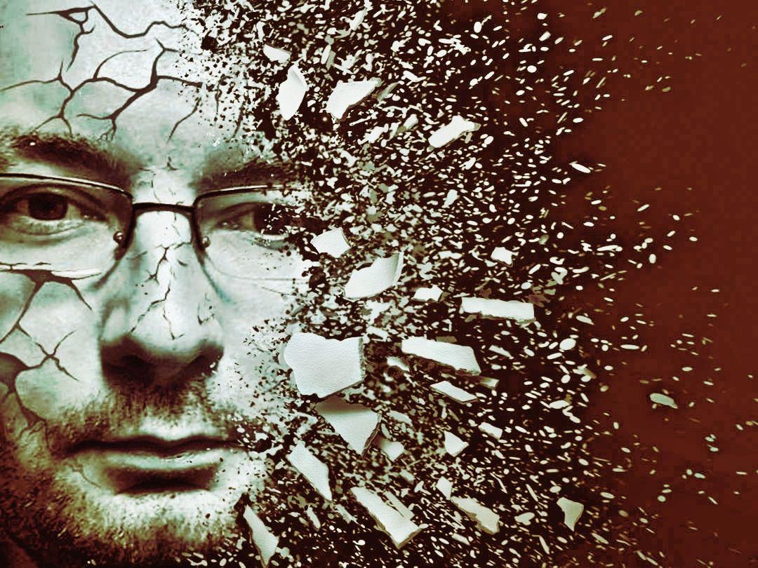 Portret mężczyzny w okularach z efektem rozpadu na fragmenty i pęknięcia na skórze, na ciemnobrązowym tle.