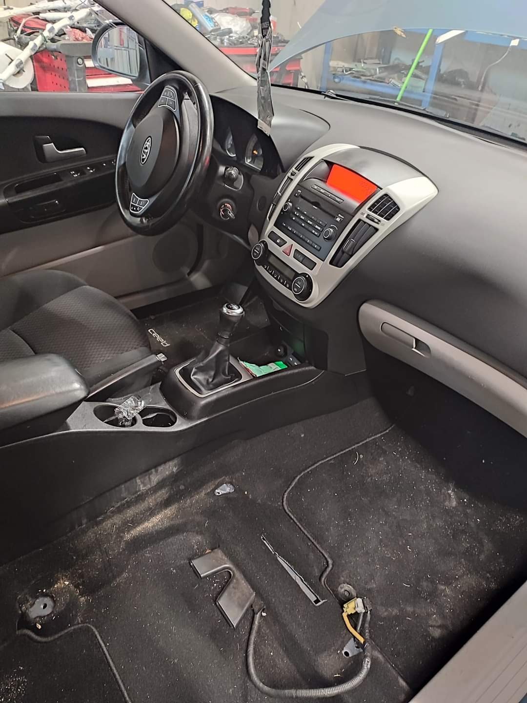 Wnętrze samochodu Kia Ceed przed czyszczeniem w Brzegu, widoczny brudny dywanik i tapicerka, zdemontowane elementy wykończenia.