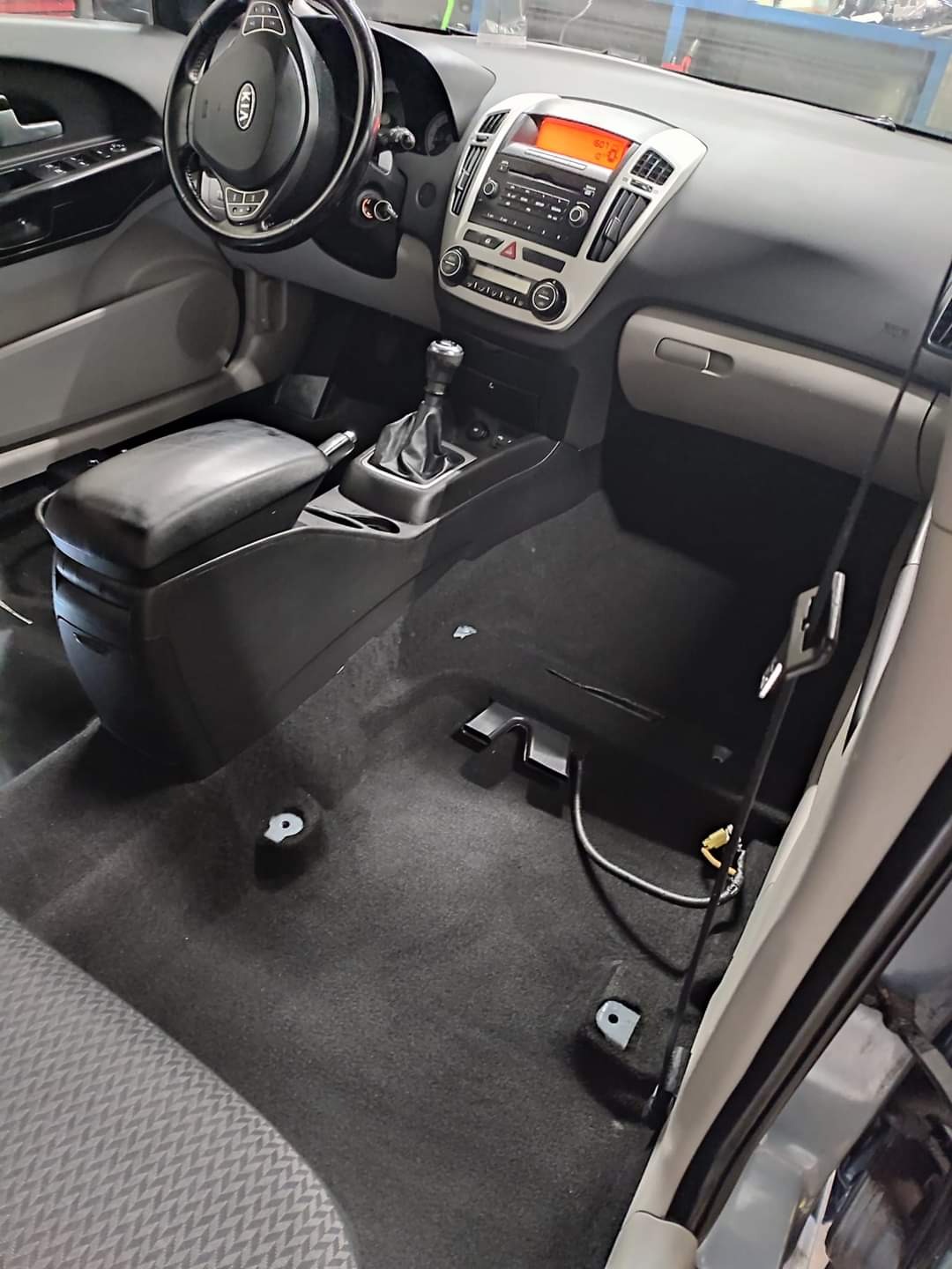 Wnętrze samochodu Kia Ceed z częściowo zdemontowaną tapicerką podłogową, widoczne elementy instalacji elektrycznej i mocowania foteli, przygotowane do prania dywanów samochodowych.