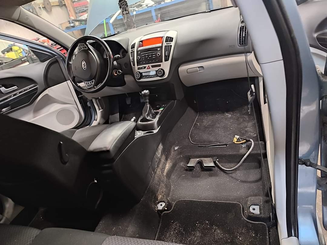 Wnętrze samochodu Kia Ceed przed czyszczeniem: widoczny brud na podłodze, brak dywaników, odsłonięte kable, otwarte drzwi, deska rozdzielcza z radiem i klimatyzacją.