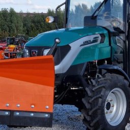 Przemysław Nowacki - Zielono-srebrny ciągnik Arbos z pomarańczowym pługiem do śniegu, widok z przodu, opony z wyraźnym bieżnikiem, w tle inne maszyny rolnicze.