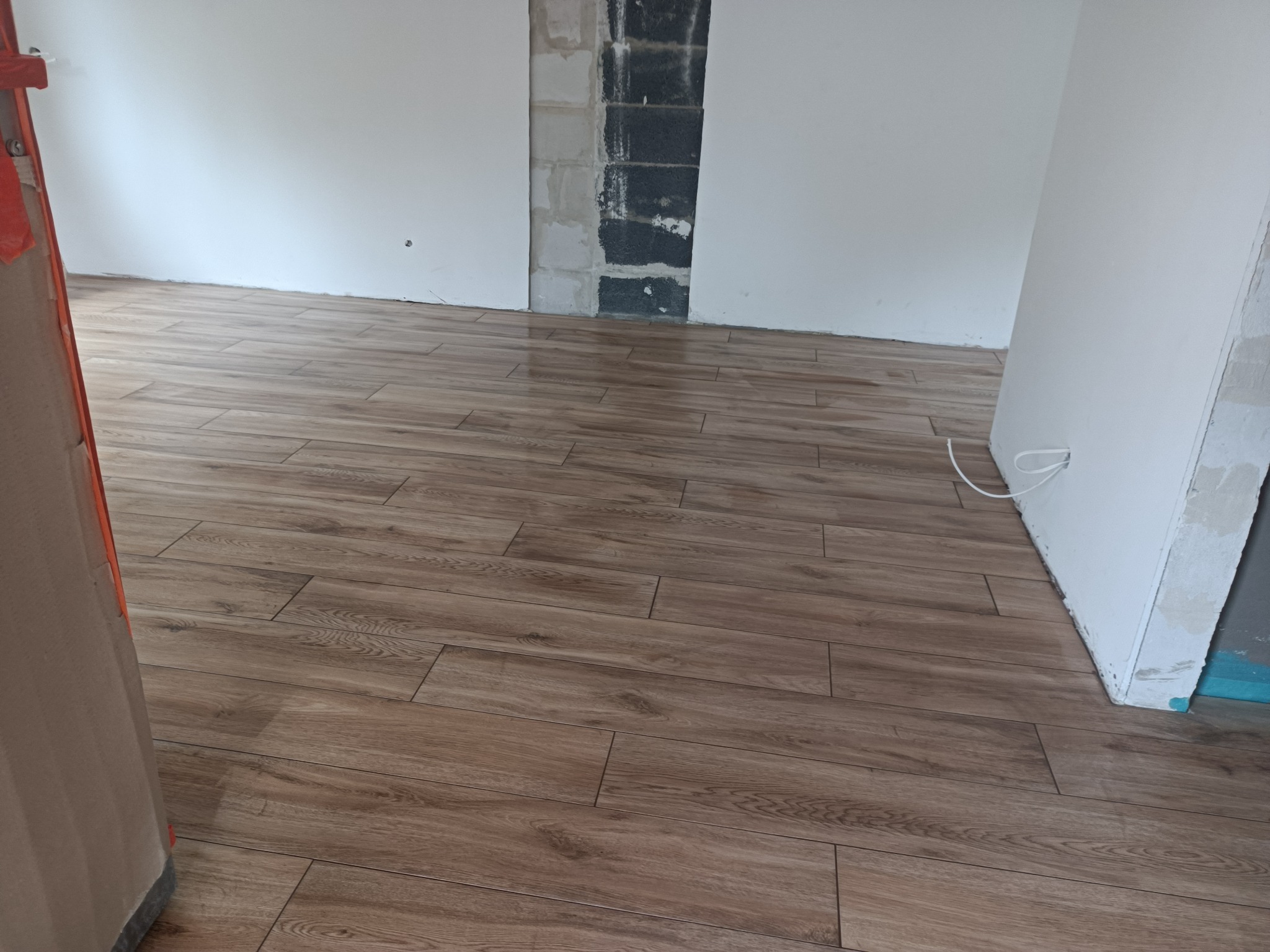 Ułożone panele podłogowe imitujące drewno w nowym wnętrzu, widoczny fragment ściany z surowym wykończeniem oraz białe ściany przygotowane do malowania.