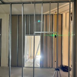 Max Construction - Montaż ścianek działowych z płyt karton-gips na metalowym stelażu, widoczny laser krzyżowy, drabina w przejściu. Etap prac wykończeniowych wnętrz.