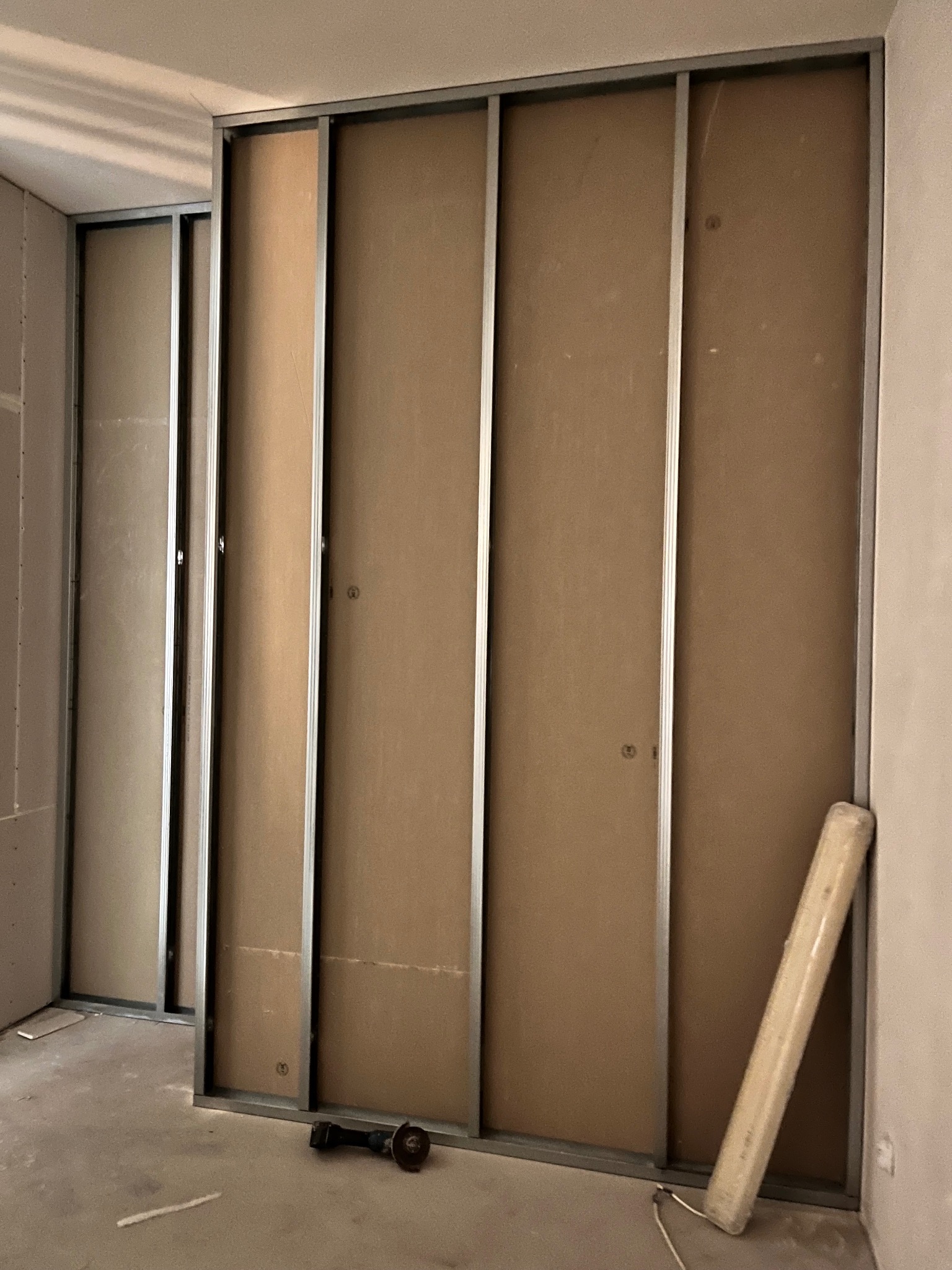 Montaż ścianki działowej z płyty kartonowo-gipsowej na metalowym stelażu, widoczny szlifierka kątowa i zwinięty materiał izolacyjny.