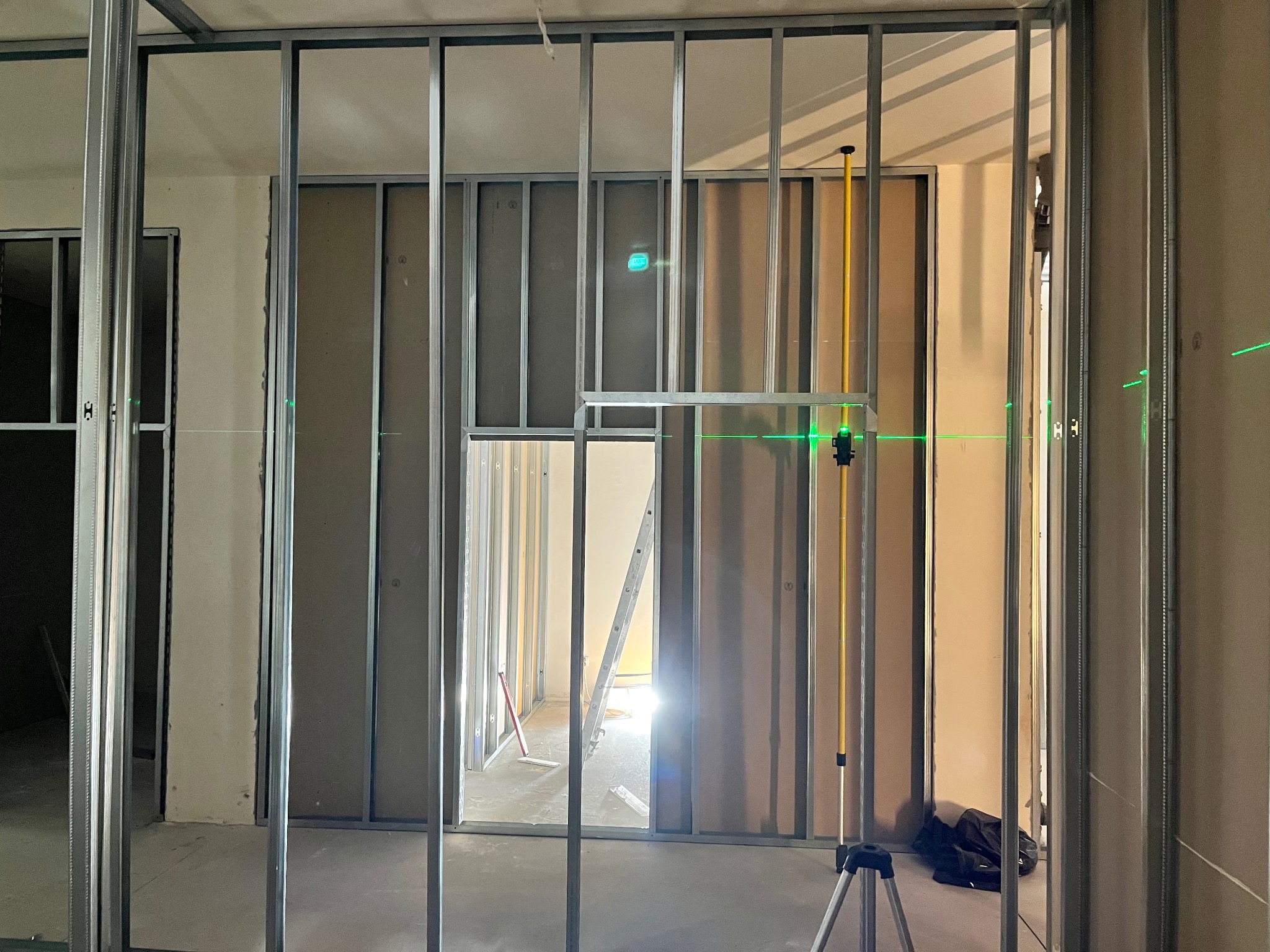 Montaż ścianek działowych z płyt karton-gips na metalowym stelażu, widoczny laser krzyżowy, drabina w przejściu. Etap prac wykończeniowych wnętrz.