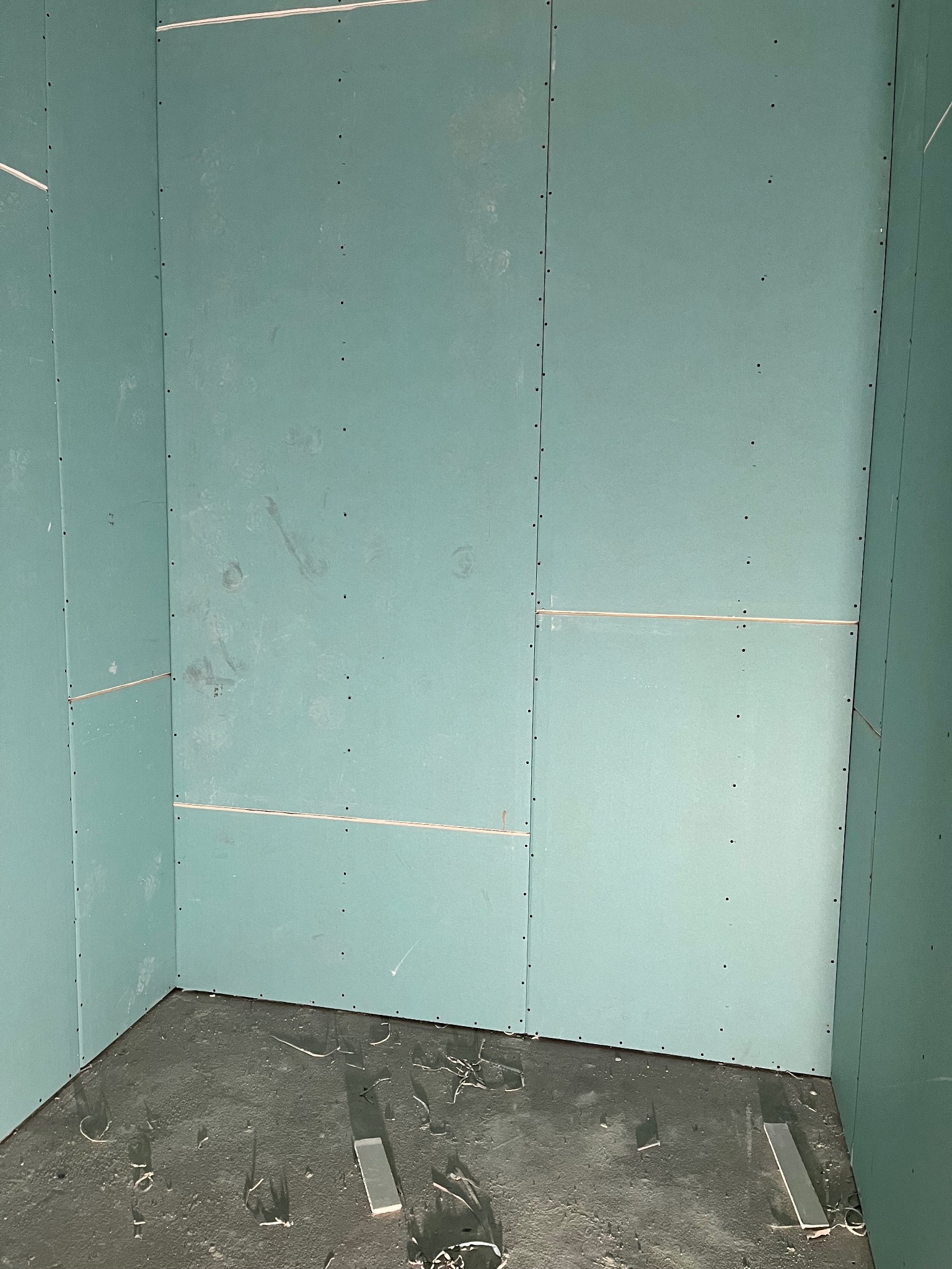 Narożnik pokoju z zamontowanymi płytami kartonowo-gipsowymi, widoczne ślady po montażu na podłodze. Szpachlowane łączenia płyt.